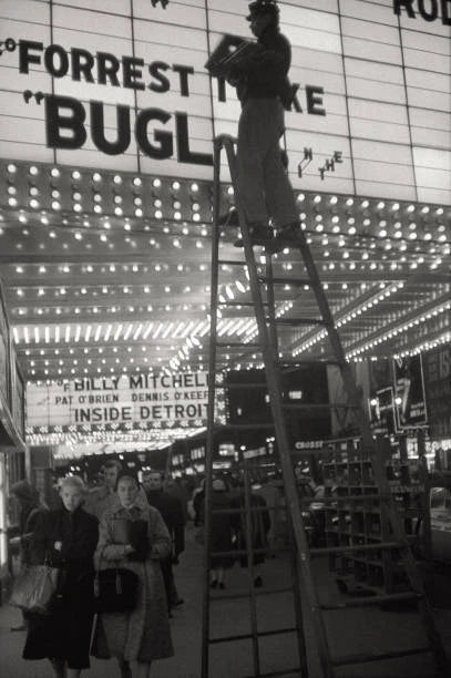 Worker changing letters cinema board up ladder among passers by Ne- Old Photo Model