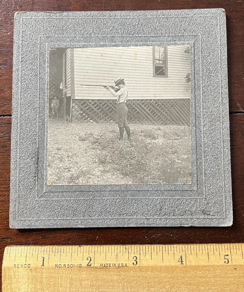 Photo on Board, Child wearing Knickers and straw hat with a rifle he's aiming. Model